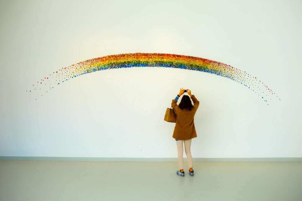 Eine Frau fotografiert eine Regenbogen-Art-Installation. Queer und BIPoc sind in meiner Praxis willkommen.
